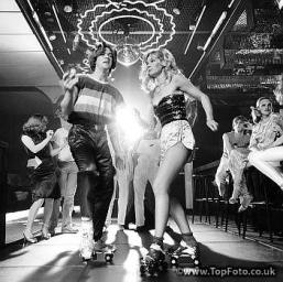 COUPLE-DISCO-DANCING-ON-ROLLER-SKATES-WEARING-TRENDY-CLOTHES-UNDER-A-MIRRORED-BALL